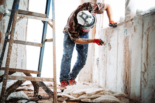 A construction worker removing spray foam on the walls of a building