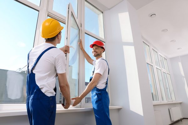 Workers in uniform installing plastic window indoors